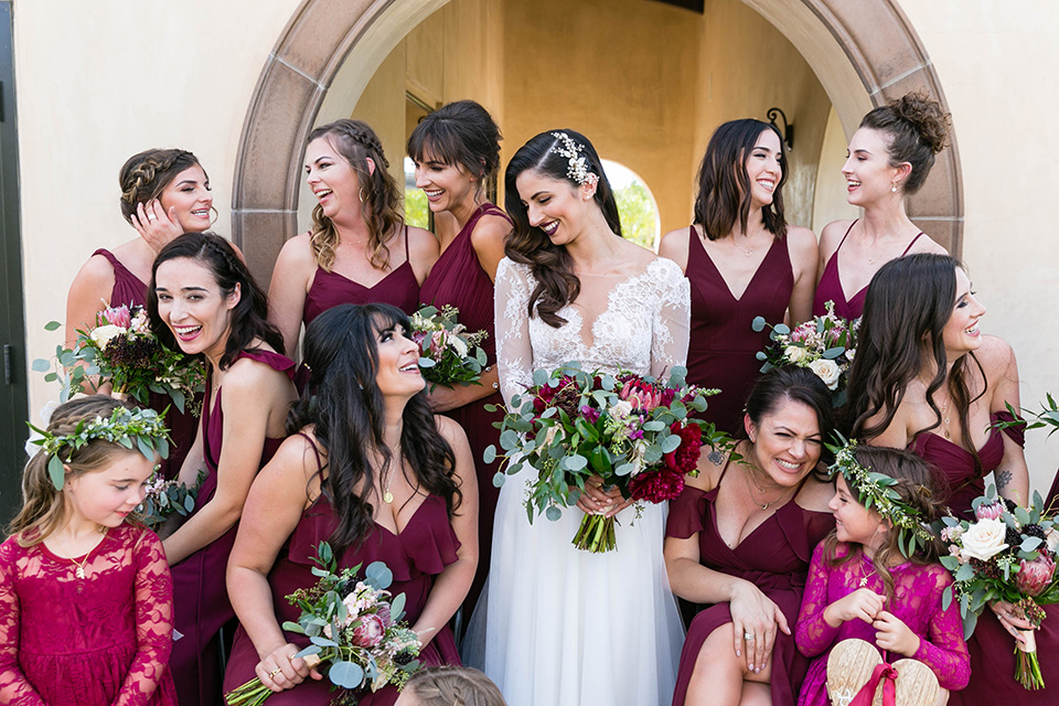  bride in a white lace gown with a full skirt and long lace sleeves and her hair in a finger wave and the bridesmaids in burgundy gowns