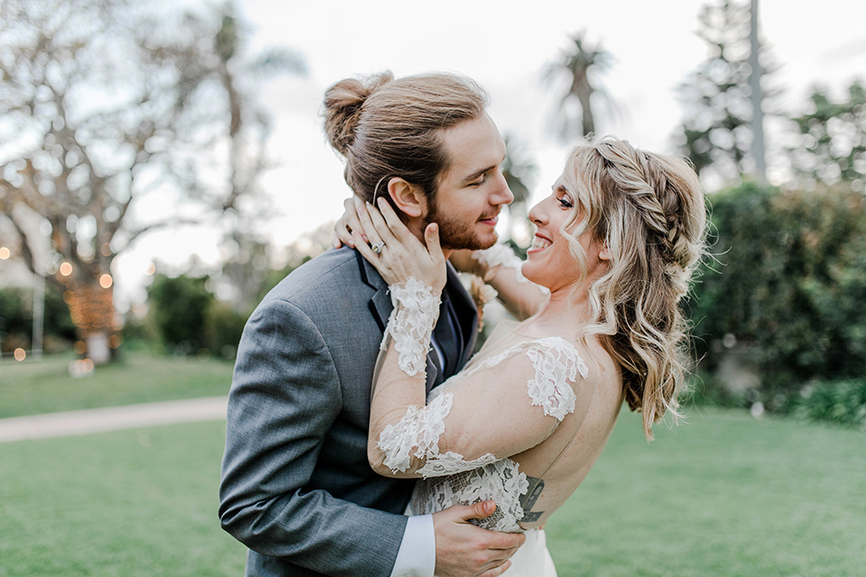 bride in a white lace gown with an illusion neckline and the groom in a grey suit with black trim and black long tie