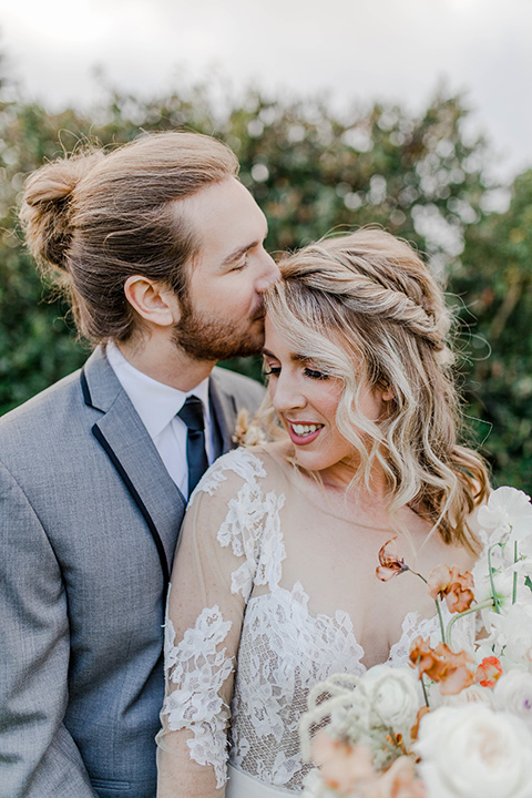 bride in a white lace gown with an illusion neckline and the groom in a grey suit with a black trim and black long tie