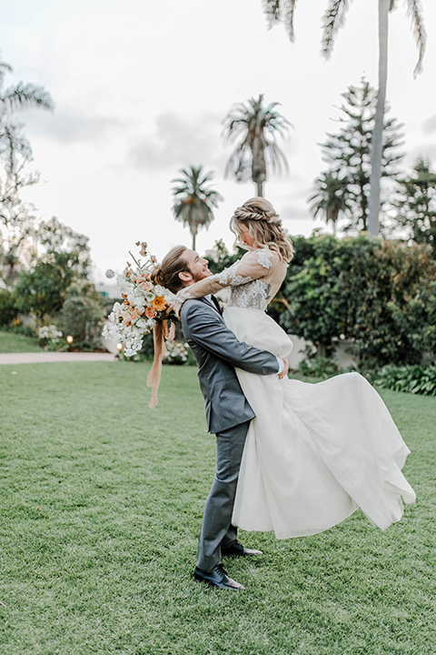 bride in a white gown with an illusion neckline hair in a loose curl, groom in a grey suit with a black trim and long black tie