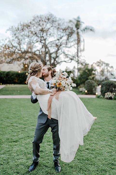 bride in a white lace gown with an illusion neckline and the groom in a grey suit with a black trim and black long tie