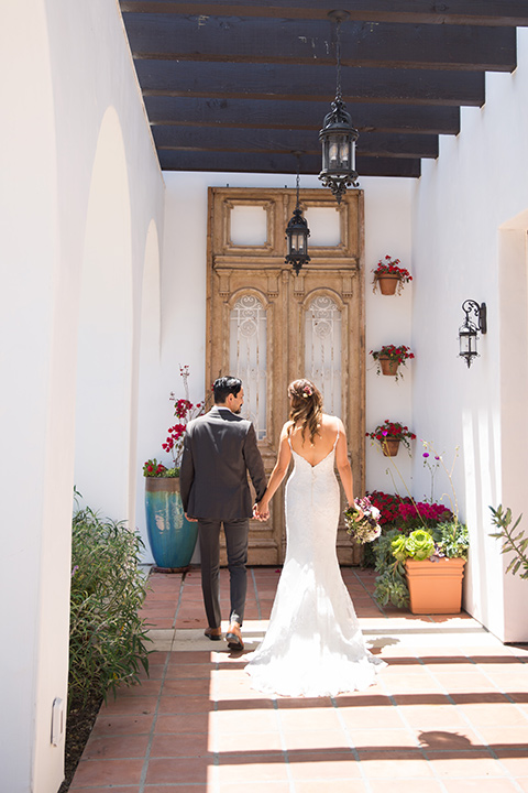 bride in a white gown with thin straps and lace detailing and the groom in a grey suit with a red long tie walking away