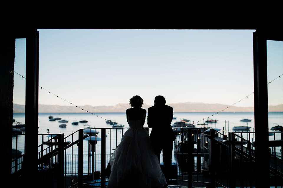 Lake Tahoe wedding bride and groom looking out window bride in a white tulle ballgown with white tulle ballgown with a strapless dresswith a strapless neckline the groom wore a navy shawl lapel tuxedo with black trim and a black bow tie