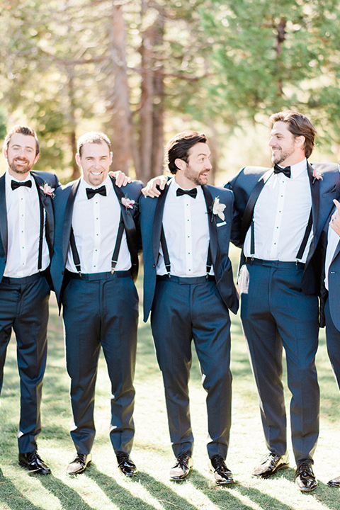 groomsmen with jackets unbuttoned in navy shawl lapel tuxedos with a black bow ties