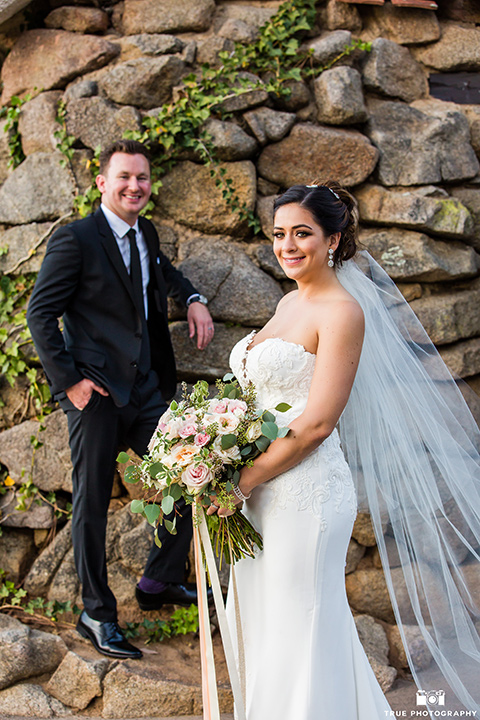 mount-woodson-castle-bride-and-groom-smiling-on-camera-groom-in-a-charcoal-suit-with-a-black-long-tie-bride-in-a-white-lace-gown-with-a-strapless-neckline