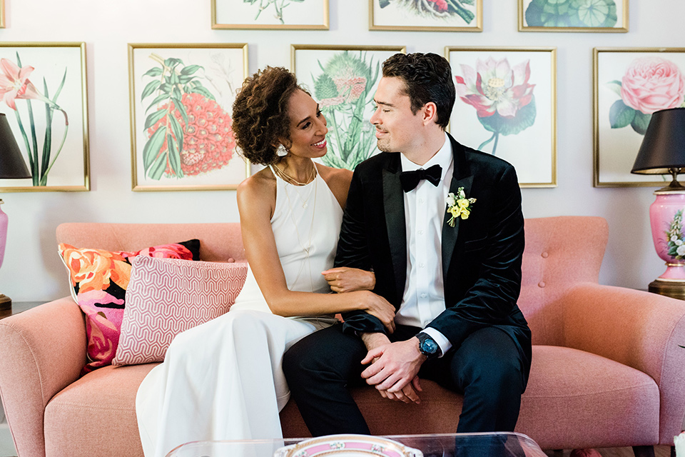 malibu-lodge-spring-wedding-shoot-bride-and-groom-on-pink-couch-bride-in-a-flowing-form-fittting-gown-with-a-high-necklink-groom-in-a-black-velvet-tuxedo-with-a-black-bow-tie