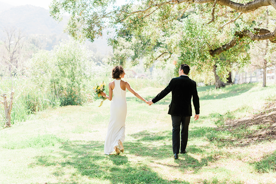 malibu-lodge-spring-wedding-shoot-bride-and-groom-walking-away-from-camera-bride-in-a-flowing-form-fittting-gown-with-a-high-necklink-groom-in-a-black-velvet-tuxedo-with-a-black-bow-tie