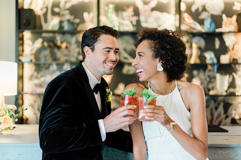 malibu-lodge-spring-wedding-shoot-bride-and-groom-with-drinks-bride-in-a-flowing-form-fittting-gown-with-a-high-necklink-groom-in-a-black-velvet-tuxedo-with-a-black-bow-tie