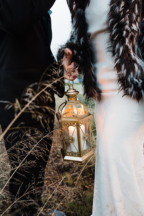 Los Robles Greens Shoot close up on lanterns bride in a bohemian style dress with a high neckline and lace with a hat groom in an all-black tuxedo look with a black shirt and bow