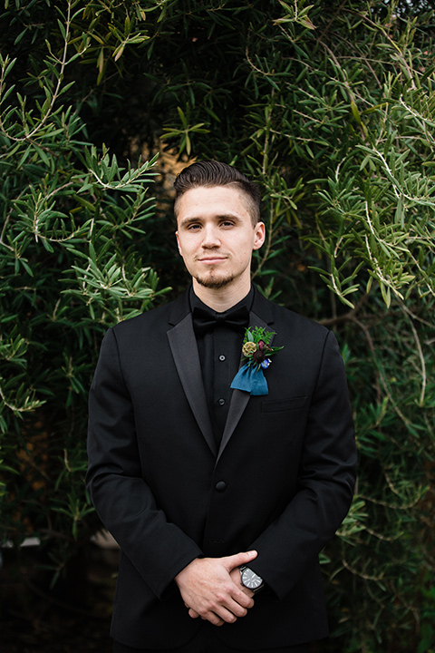 groom standing alone in an all black tuxedo look with a black shirt and bow