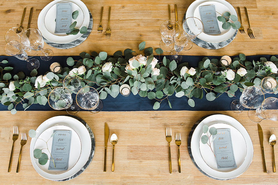 Los Robles Greens Shoot table decor and flatware with white plates and gold flatware on a wooden table with green florals and table runner