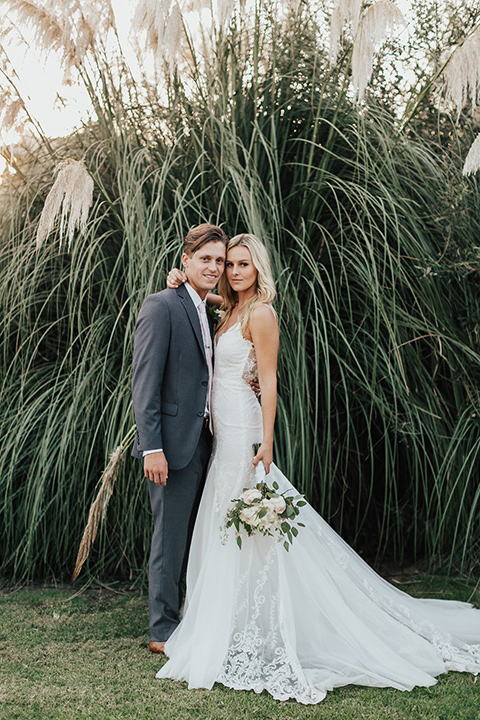 monarch-beach-resort-bride-and-groom-in-front-of-plants-bride-in-a-lace-dress-with-thin-straps-groom-in-a-grey-suit-with-ivory-long-tie