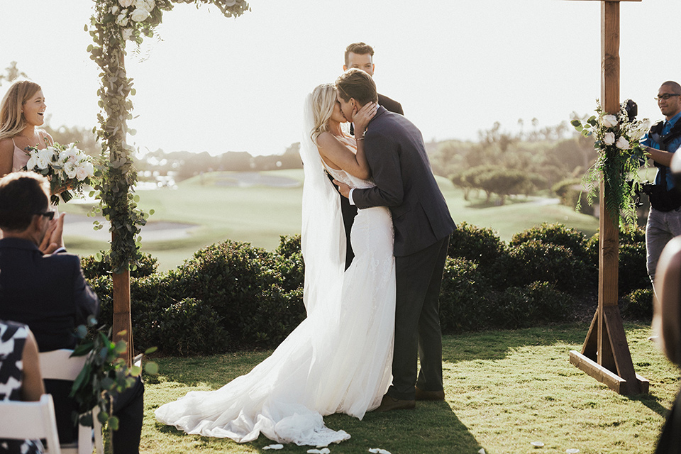 monarch-beach-resort-ceremony-kiss-bride-in-a-lace-dress-with-thin-straps-groom-in-a-grey-suit-with-ivory-long-tie