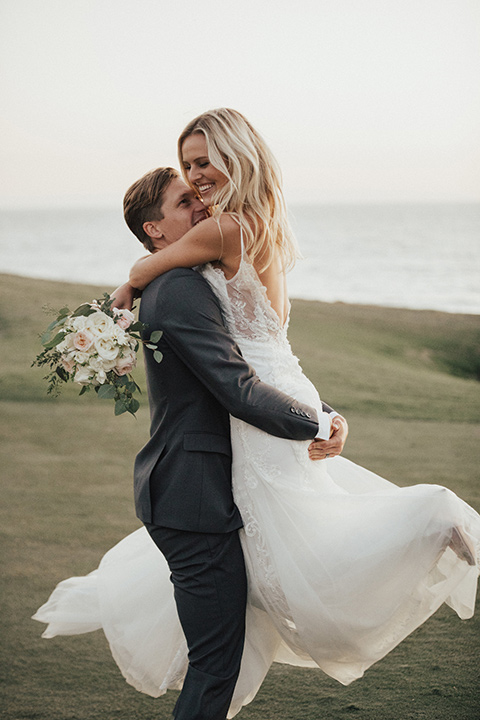 monarch-beach-resort-groom-picking-up-bride-bride-in-a-lace-dress-with-thin-straps-groom-in-a-grey-suit-with-ivory-long-tie