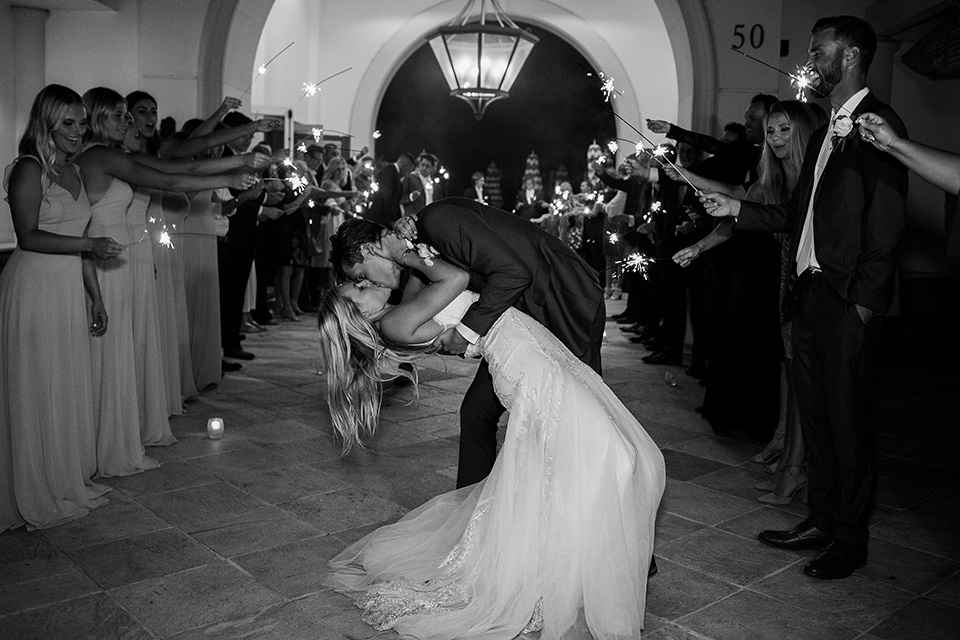 monarch-beach-resort-kiss-with-sparlers-bride-in-a-lace-dress-with-thin-straps-groom-in-a-grey-suit-with-ivory-long-tie