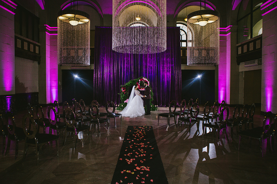 majestic-downtown-los-angeles-shoot-bride-and-groom-at-ceremony-bride-and-groom-close-embrace-bride-in-a-tulle-ballgown-with-a-beaded-bodice-with-long-sleeves-in-a-burgundy-tuxedo-in-a-shawl-lapel-and-black-bow-tie