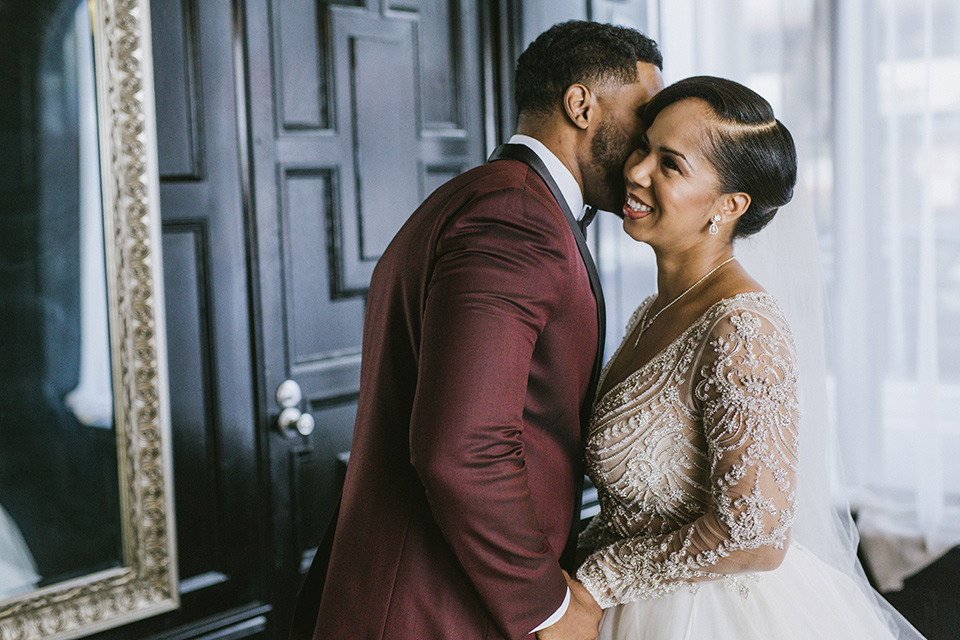 majestic-downtown-los-angeles-shoot-bride-and-groom-smiling-and-laughing-close-bride-and-groom-close-embrace-bride-in-a-tulle-ballgown-with-a-beaded-bodice-with-long-sleeves-groo-in-a-burgundy-tuxedo-with-a-satin-lapel-and-black-bow-tie