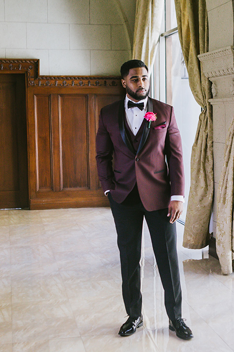 majestic-downtown-los-angeles-shoot-groom-standing-alone-in-a-burgundy-tuxedo-with-a-black-shawl-lapel-and-black-bow-tie