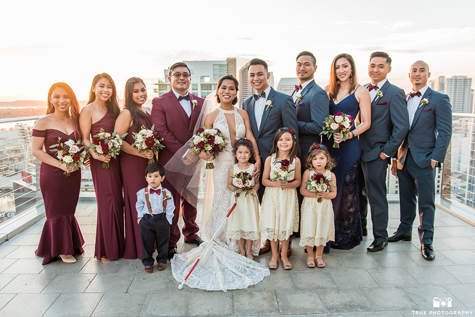 skybox-real-wedding-bridal-arty-by-windows-bride-wearing-a-fitting-lace-dress-with=straps-groom-wearing-a-blue-suit-bridesmaids-in-burgundy-groomsmen-in-blue