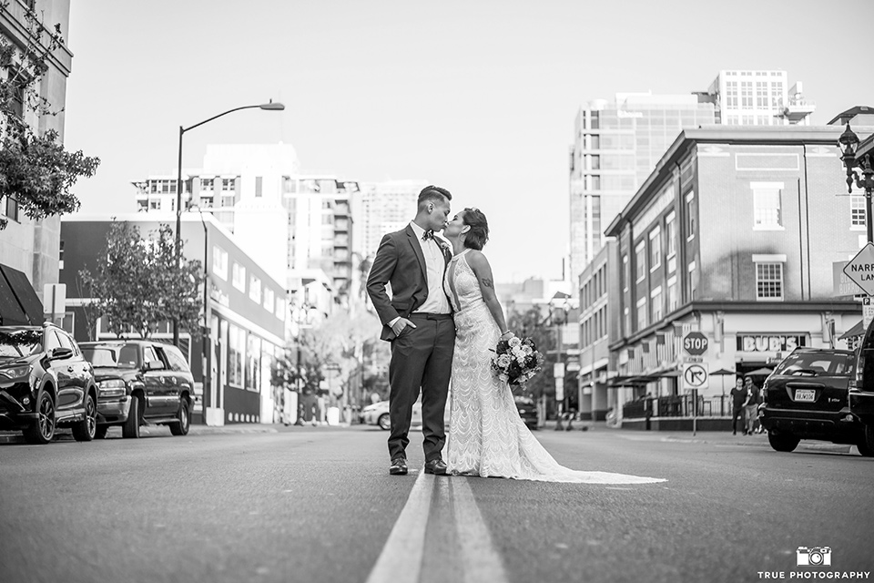 skybox-real-wedding-bride-and-groom-kissing-in-the-street-bride-wearing-a-fitting-lace-dress-with=straps-groom-wearing-a-blue-suit-bridesmaids-in-burgundy-groomsmen-in-blue