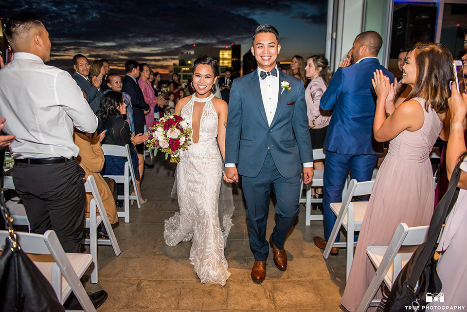 skybox-real-wedding-end-of-the-ceremony-bride-wearing-a-fitting-lace-dress-with=straps-groom-wearing-a-blue-suit-bridesmaids-in-burgundy-groomsmen-in-blue