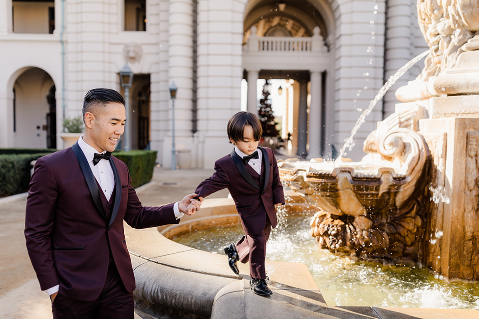 Maternity-workshop-father-and-son-walking-dad-wearing-a-burgundy-tuxedo-and-black-bow-tie-little-boy-wearing-a-burgundy-tux-that-matches-his-father