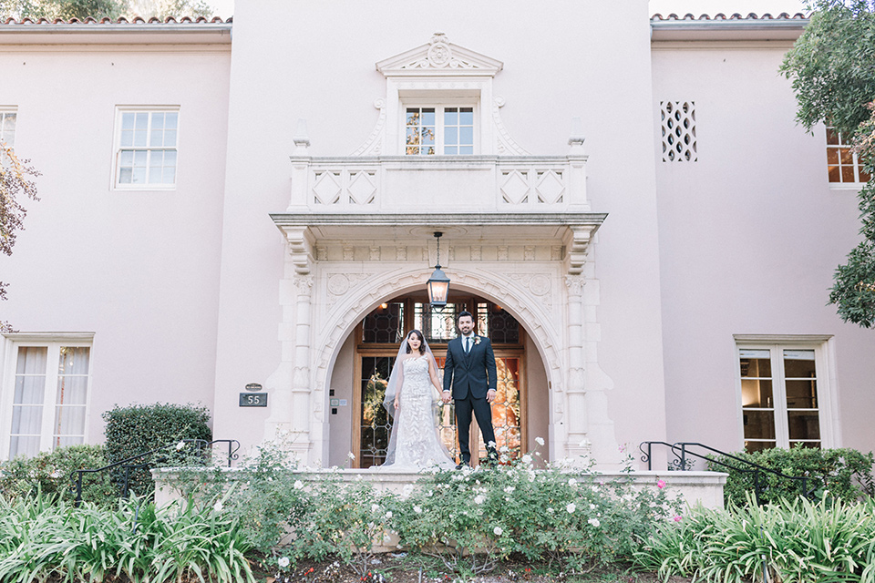 Maxwell-House-Shoot-bride-and-groom-standing-outside-venue-bride-in-a-trendy-gown-with-an-illusion-bodice-and-strapless-neckline-groom-in-a-black-suit-with-a-long-black-tie