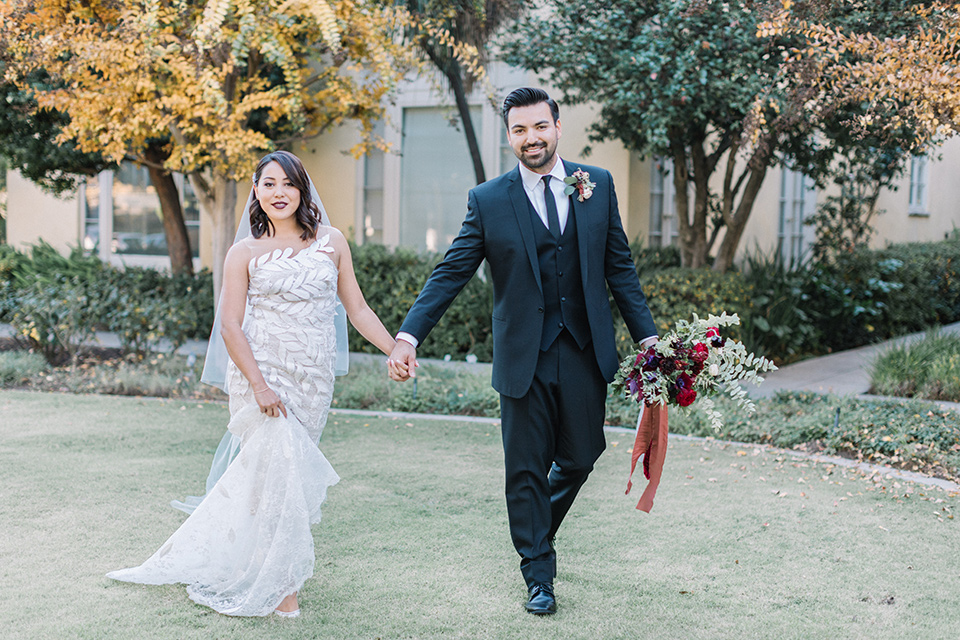 Maxwell-House-Shoot-bride-and-groom-walking-on-grass-bride-in-a-trendy-gown-with-an-illusion-bodice-and-strapless-neckline-groom-in-a-black-suit-with-a-long-black-tie