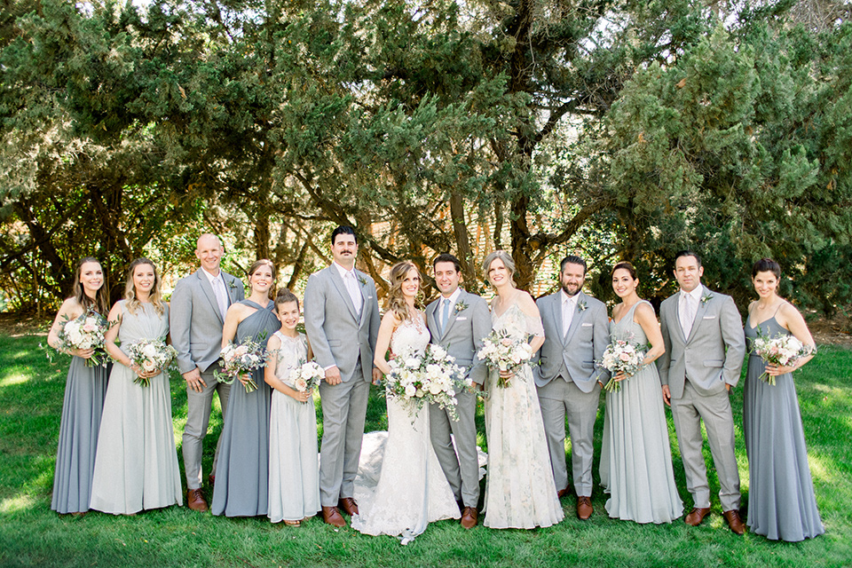 Temecula-Creek-Inn-Wedding-bridal-party-bridesmaids-in-various-dusty-blue-dresses-groomsmen-in-light-grey-suits-with-blue-suits-bride-in-a-form-fitting-lace-gown-with-an-illusion-back-detail-groom-in-a-light-grey-suit-with-a-light-blue-polka-dot-tie