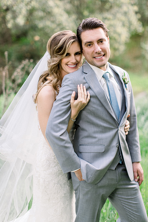 Temecula-Creek-Inn-Wedding-bride-and-groom-looking-at-camera-bride-in-a-forfitting-lace-gown-with-an-illusion-back-detai-groom-in-a-light-grey-suit-with-light-blue-polka-dot-tiel