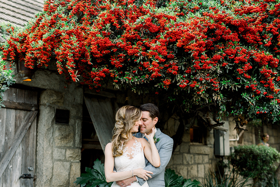 Temecula-Creek-Inn-Wedding-bride-and-groom-under-bougainvillea-bride-in-a-form-fitting-lace-gown-with-an-illusion-back-detail-groom-in-a-light-grey-suit-with-a-light-blue-polka-dot-tie