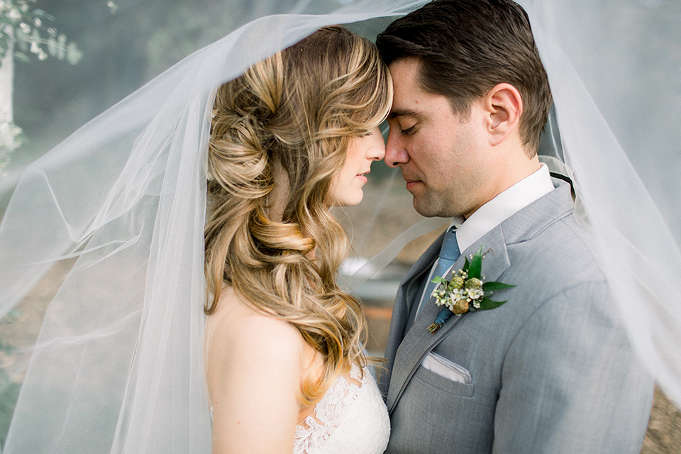 Temecula-Creek-Inn-Wedding-bride-and-groom-under-veil-bride-in-a-form-fitting-lace-gown-with-an-illusion-back-detail-groom-in-a-light-grey-suit-with-a-light-blue-polka-dot-tie