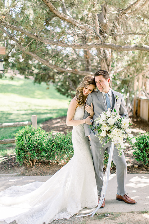 Temecula-Creek-Inn-Wedding-bride-resting-head-on-groom-groom-holding-flowers-bride-in-a-lace-dress-with-an-illusion-back-groom-in-a-light-grey-suit-with-blue-patterned-tie