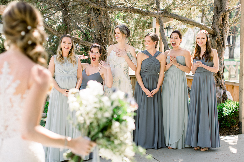 Temecula-Creek-Inn-Wedding-bridesmaids-see-bride-for-the-first-time-bride-in-a-form-fitting-lace-gown-with-an-illusion-back-detail-bridesmaids-in-different-shades-of-dusty-blue-dresses