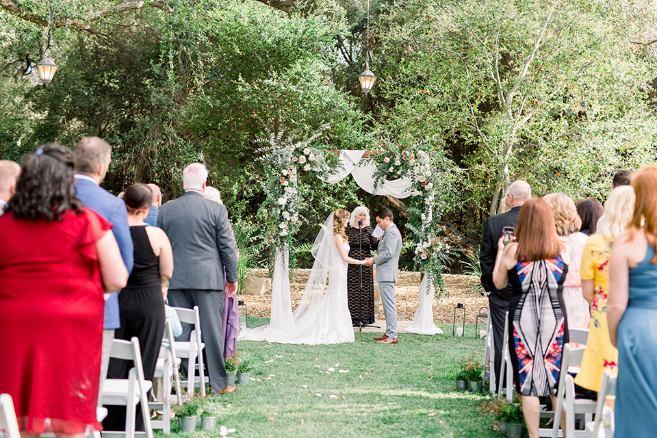 Temecula-Creek-Inn-Wedding-ceremony-space-bride-in-a-form-fitting-lace-gown-with-an-illusion-back-detail-groom-in-a-light-grey-suit-with-a-light-blue-polka-dot-tie