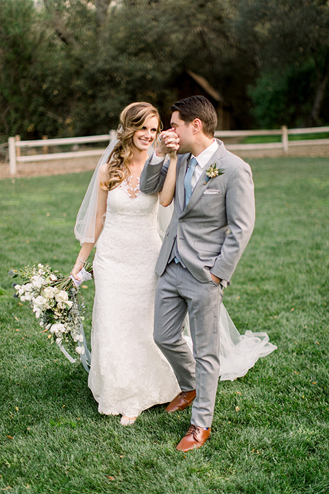 Temecula-Creek-Inn-Wedding-groom-kissing-brides-hand-bride-in-a-forfitting-lace-gown-with-an-illusion-back-detai-groom-in-a-light-grey-suit-with-light-blue-polka-dot-tiel