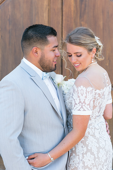  bride in a lace formfitting gown with an illusion neckline the groom in a light grey suit and bow tie 