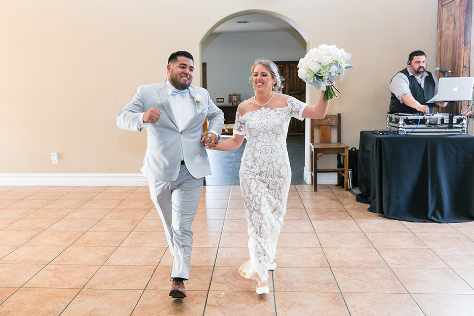 bride in a lace formfitting gown with an illusion neckline the groom in a light grey suit and bow tie 