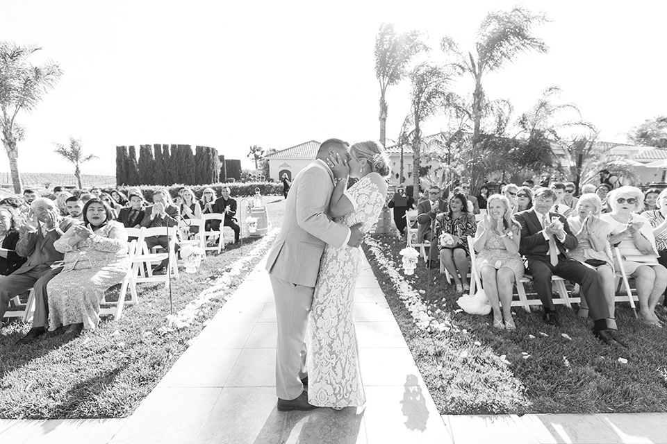 bride in a lace formfitting gown with an illusion neckline the groom in a light grey suit and bow tie 