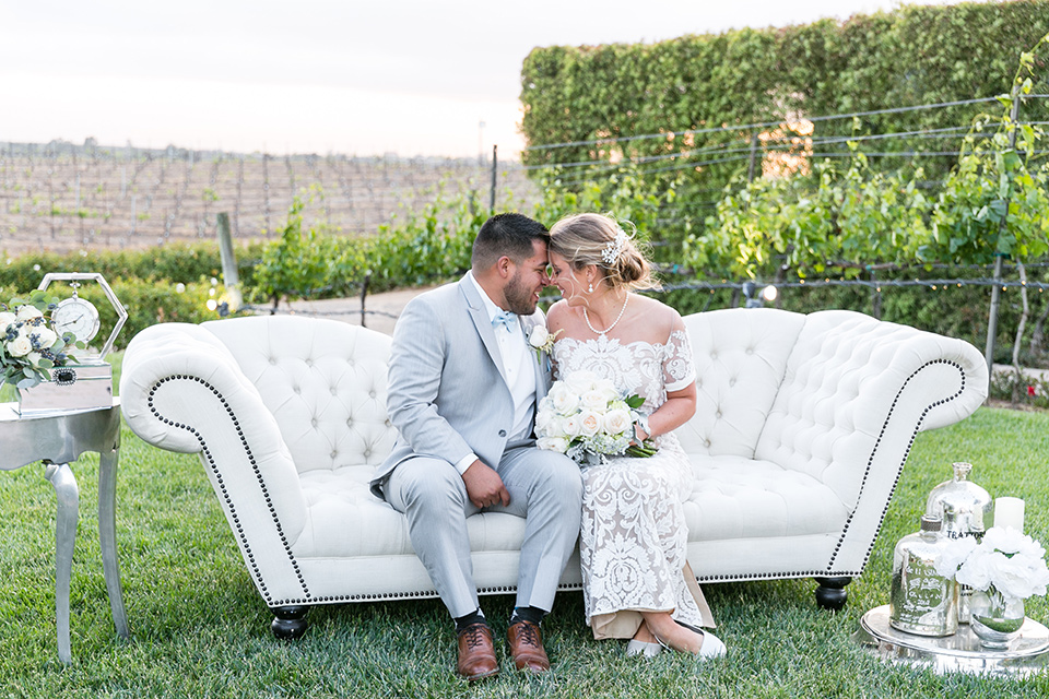 bride in a lace formfitting gown with an illusion neckline the groom in a light grey suit and bow tie 