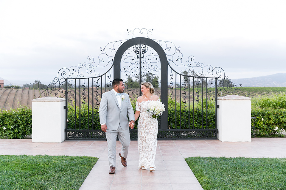 bride in a lace formfitting gown with an illusion neckline the groom in a light grey suit and bow tie 