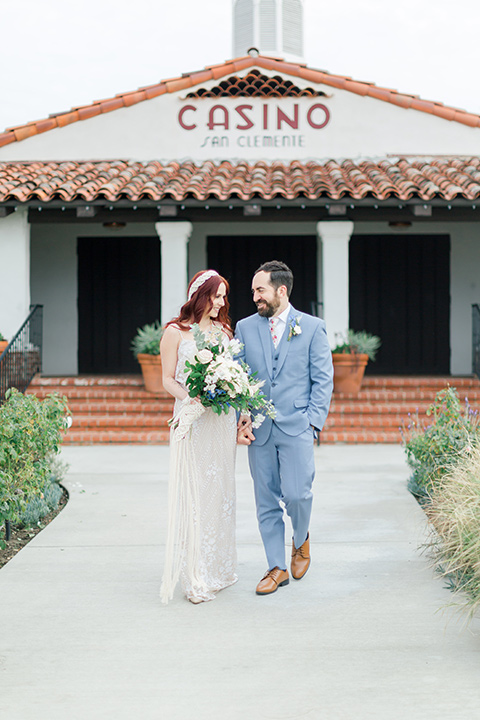  bride in a cream form fitting lace gown with a macramé headpiece groom in a light blue suit with a floral neck tie