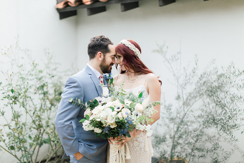  bride in a cream form fitting lace gown with a macramé headpiece, groom in a light blue suit with a floral tie