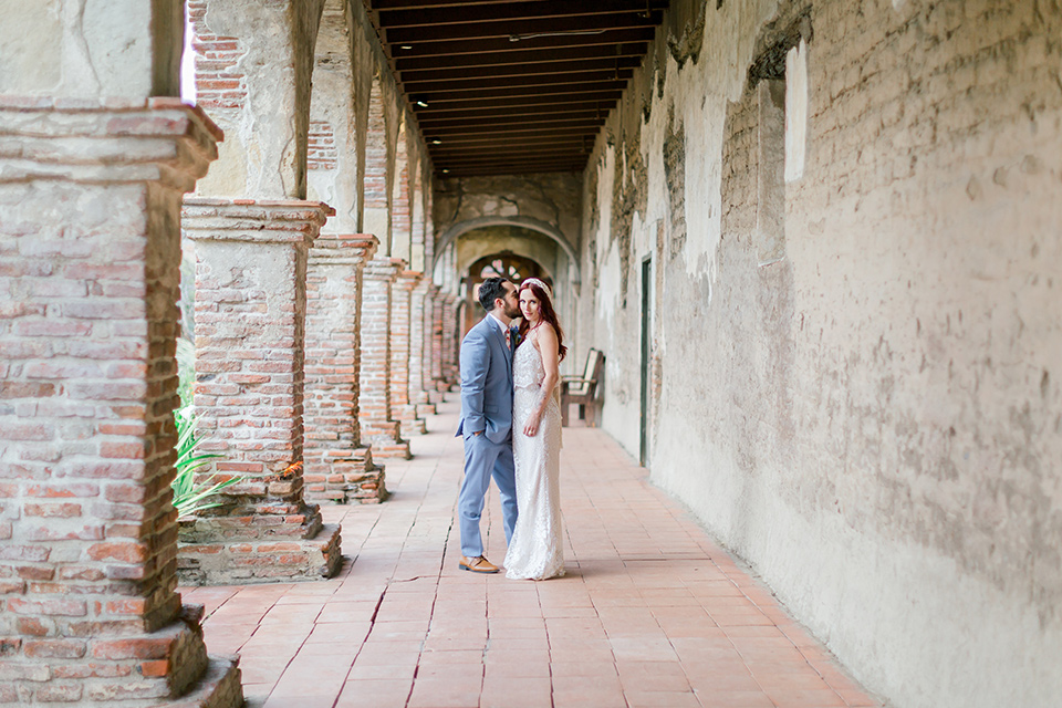  bride in a cream form fitting lace gown with a macramé headpiece, groom in a light blue suit with a floral tie