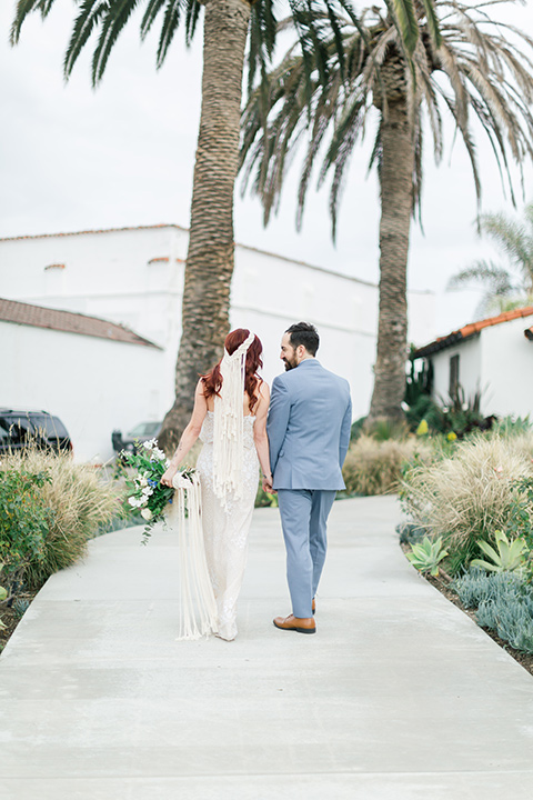  bride in a cream form fitting lace gown with a macramé headpiece groom in a light blue suit with a floral neck tie 