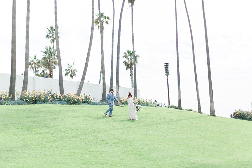  bride in a cream form fitting lace gown with a macramé headpiece, groom in a light blue suit with a floral tie