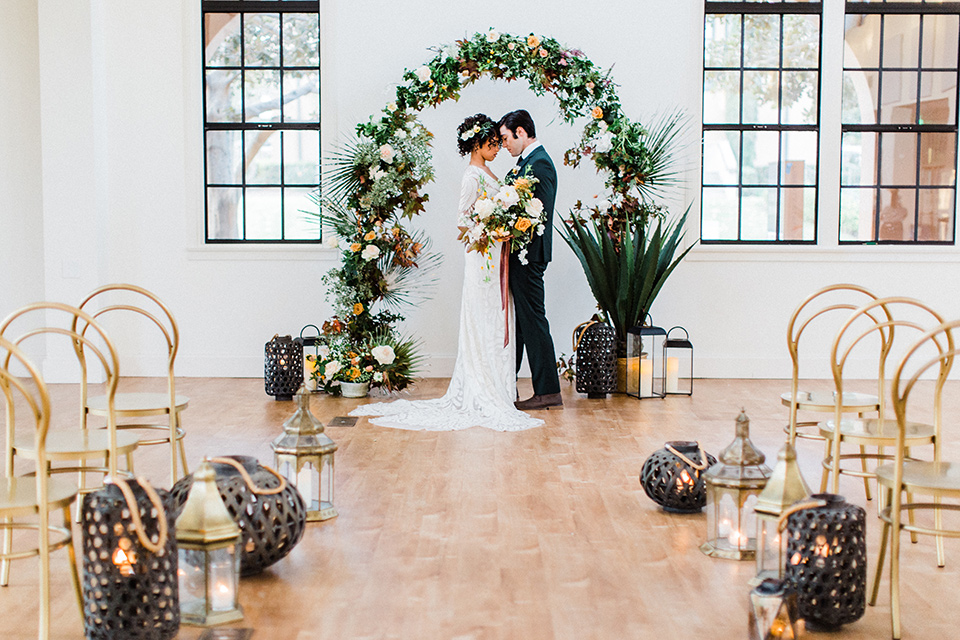 modern Moroccan shoot bride and groom at ceremony space the bride in a white lace gown with long sleeves and a v neck line and the groom is in a green suit with a brown long tie