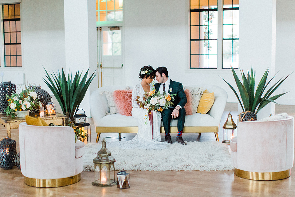 modern Moroccan shoot bride and groom on the couch at the reception the bride in a white lace gown with long sleeves and a v neck line and the groom is in a green suit with a brown long tie