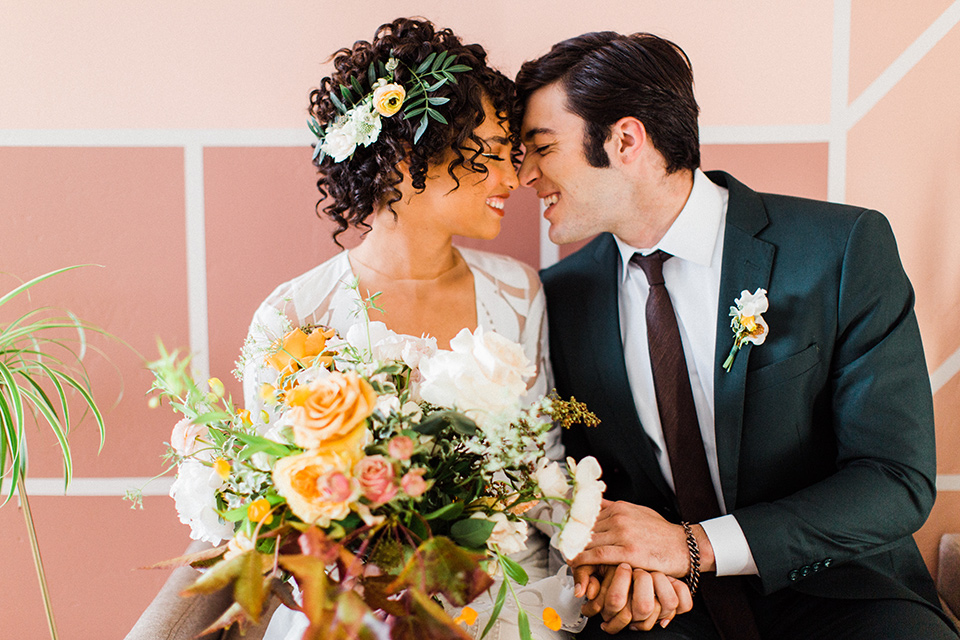 modern Moroccan shoot bride and groom on the couch at the reception close up the bride in a white lace gown with long sleeves and a v neck line and the groom is in a green suit with a brown long tie