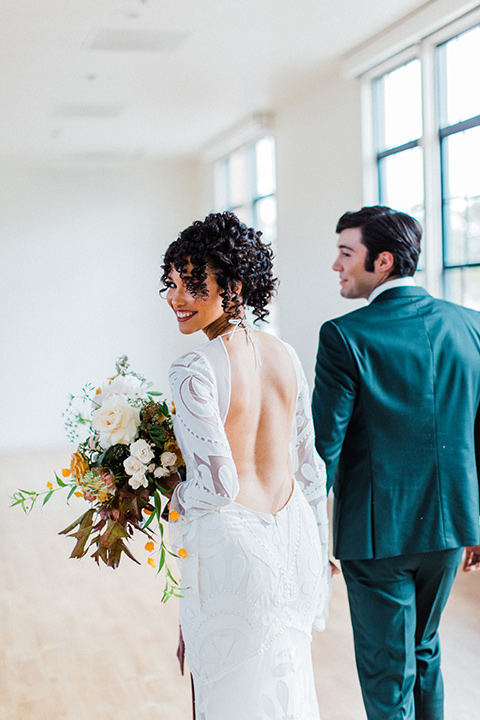 modern Moroccan shoot bride and groom walking by the windows the bride in a white lace gown with long sleeves and a v neck line and the groom is in a green suit with a brown long tie